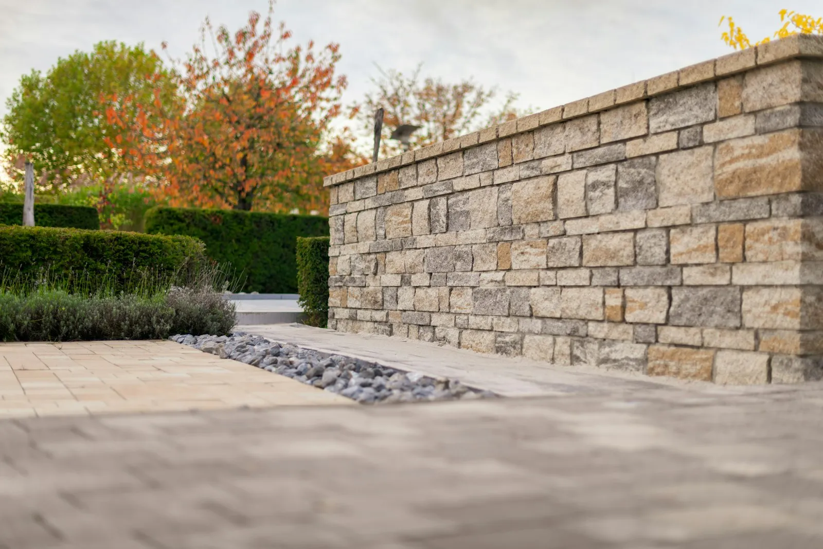 A tall stacked-stone wall beside a paved terrace with clipped hedges